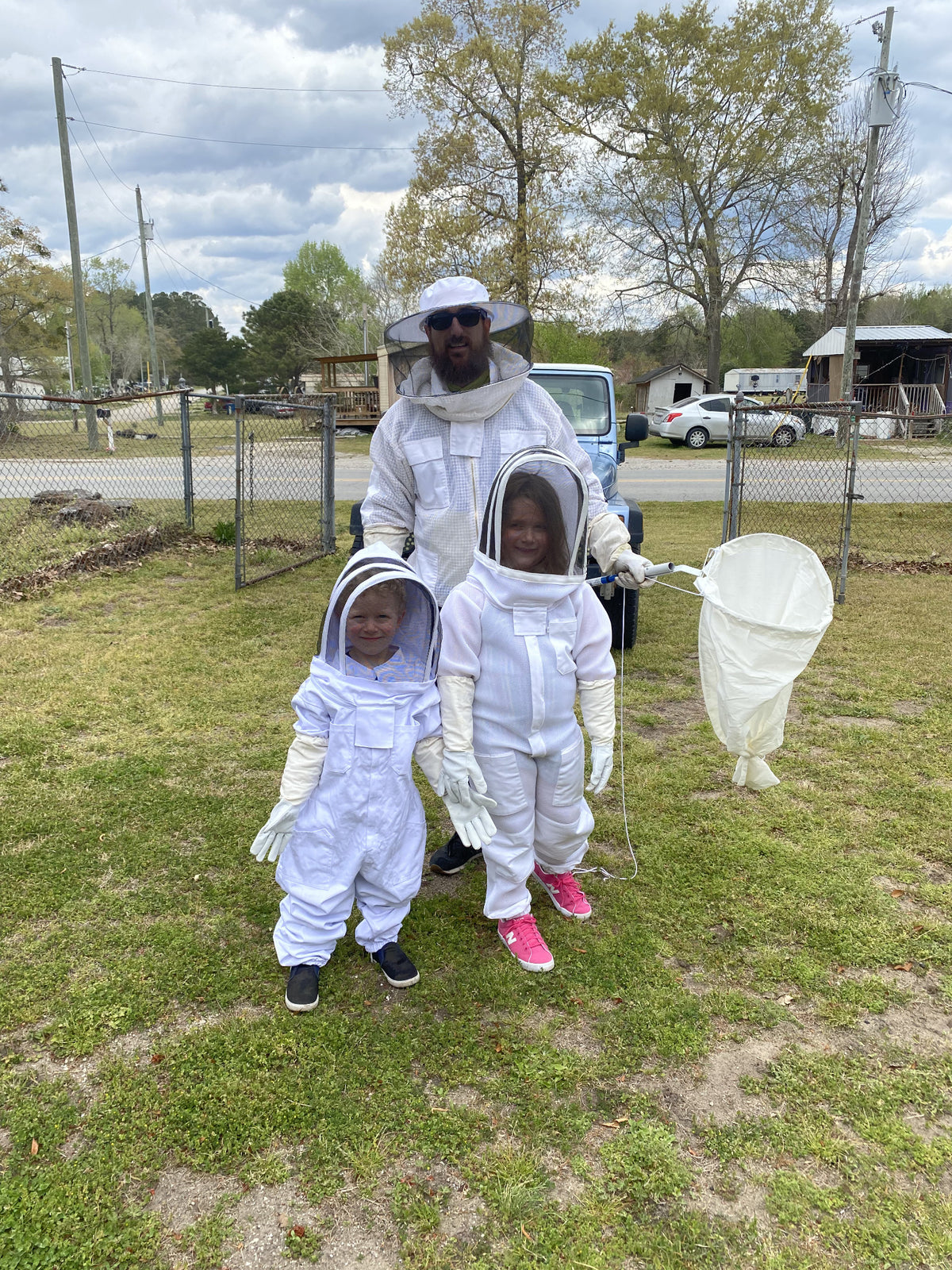 Matthew Hooker and his children in beekeeping suits with a swarm-catching net
